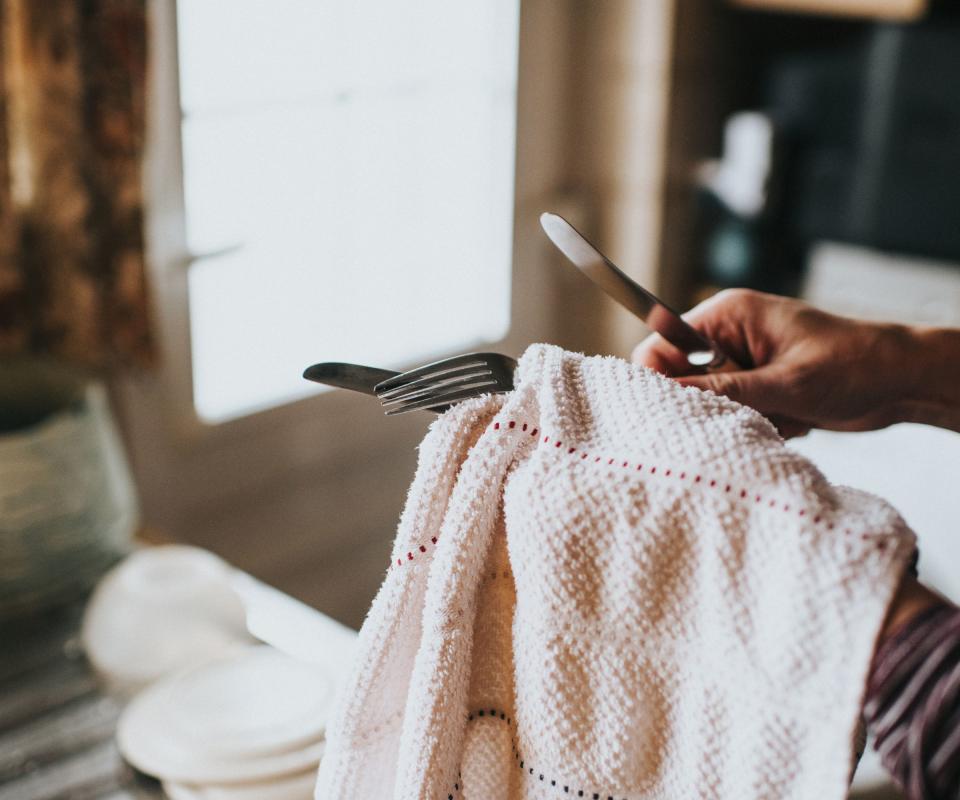 Someone using a pink towel to dry silver cutlery