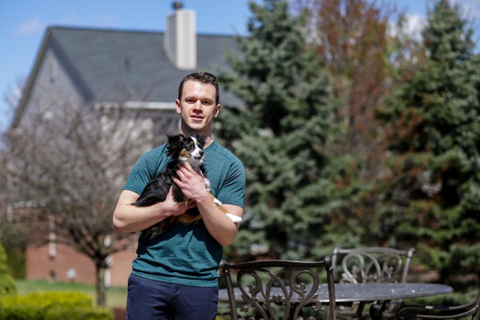 Andrew Dolenga, 22, is a senior at Michigan State University, where he is getting a degree in mechanical engineering. Dolenga holds his dog, Tucker, at his parent's home in Rochester, Michigan, on April 8. He is now taking his classes online, but is still forced to pay his rent for his off-campus apartment even though he longer resides there.