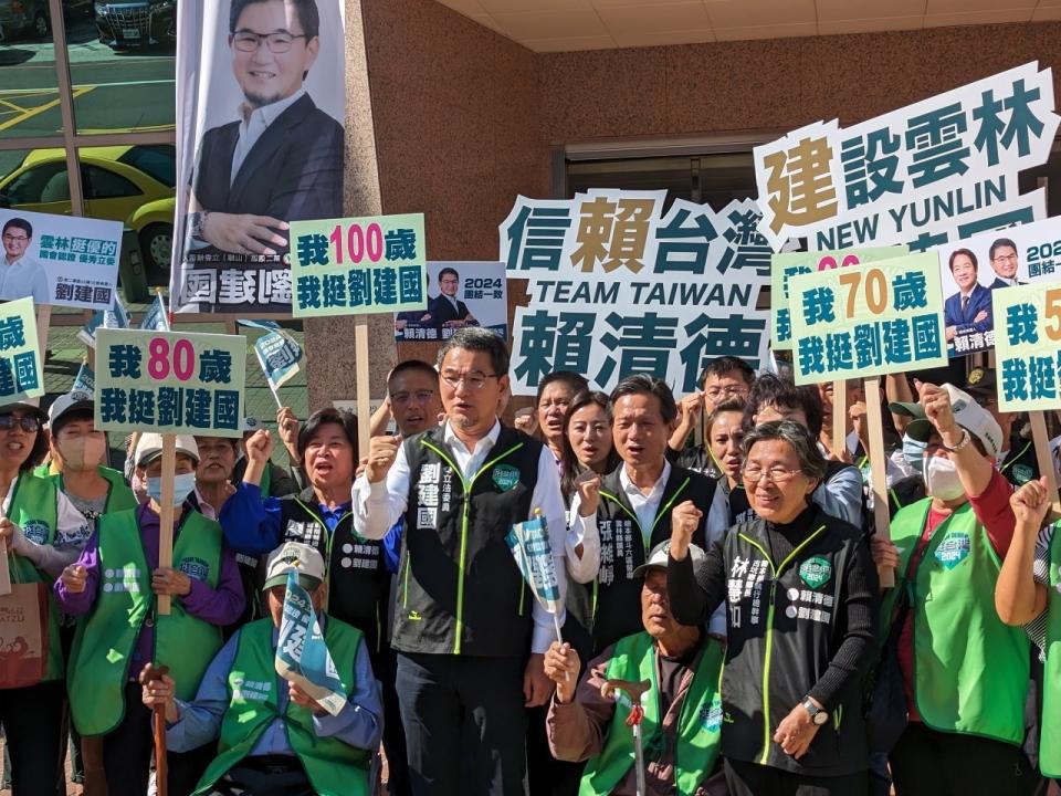 ▲民進黨提名競選連任立委劉建國(中)與二十歲到一ＯＯ歲組成的全世代與黨公職以及眾多支持者陪同下在選委會門前持牌信賴台灣賴清德、我廷劉建國等舉牌，高喊劉建國加油、當選。(記者劉春生攝)