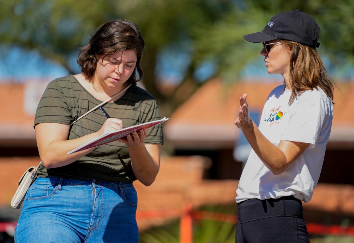 Brittany Dover (left) signs a petition while Sarah Liguori explains the issue outside of the Burton Barr Library and voting center on Aug. 2, 2022, in Phoenix.
