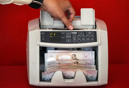 A pawn shop worker uses a machine to count Thai Baht banknotes as he prepares to purchase items from customers at Easy Money Pawn shop in Bangkok, August 27, 2013. REUTERS/Athit Perawongmetha