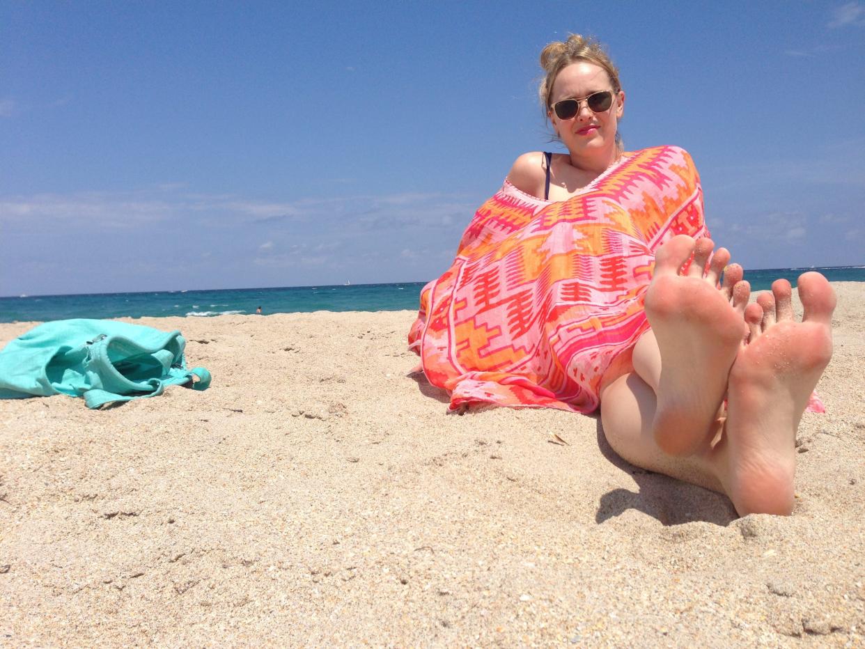 A woman sitting on the beach wearing a brightly colored coverup next to a turquoise bag.