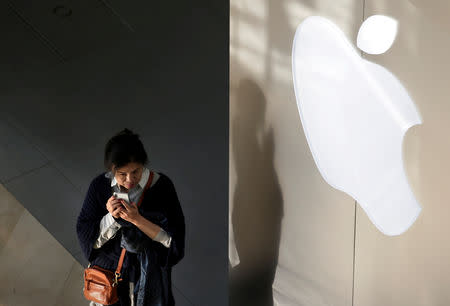 FILE PHOTO: A woman holds her phone near an Apple company logo in Beijing, China December 14, 2018. REUTERS/Jason Lee