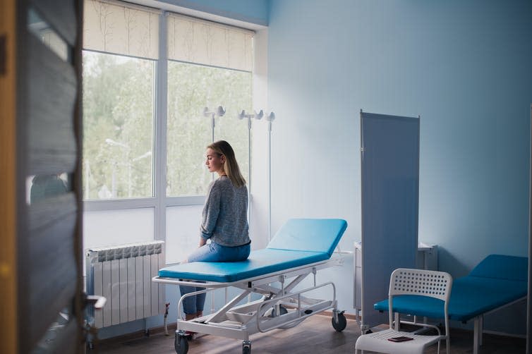 Young woman sitting on a hospital bed waits alone in an examination room.