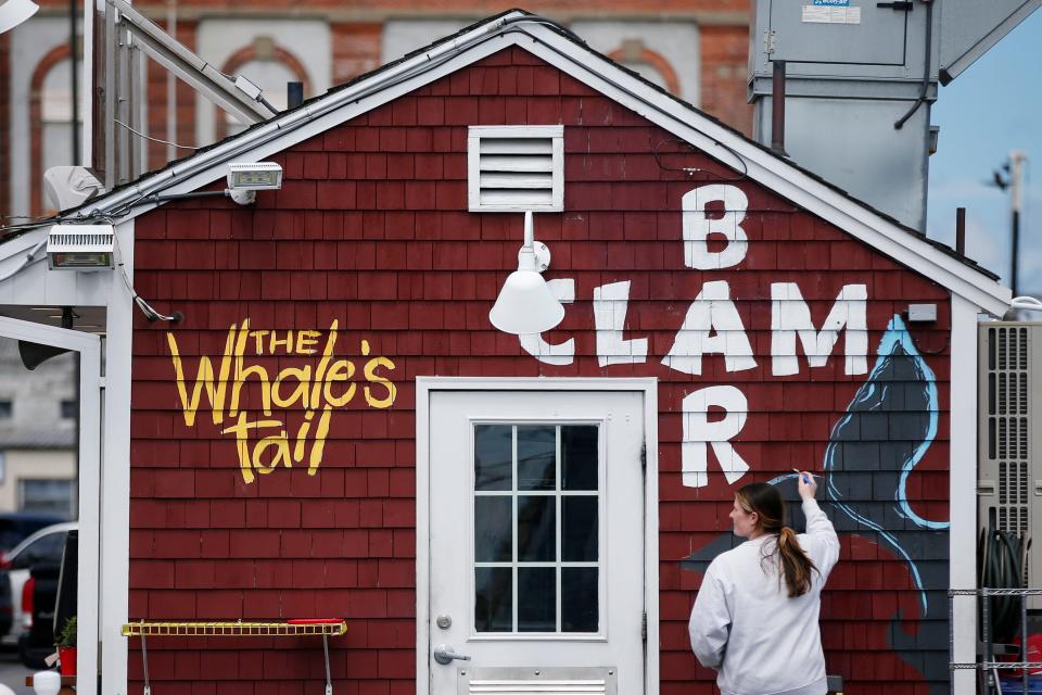 Kailey Humason paints the tale of a whale on the side of The Whale's Tail Clam Bar on New Bedford's waterfront.