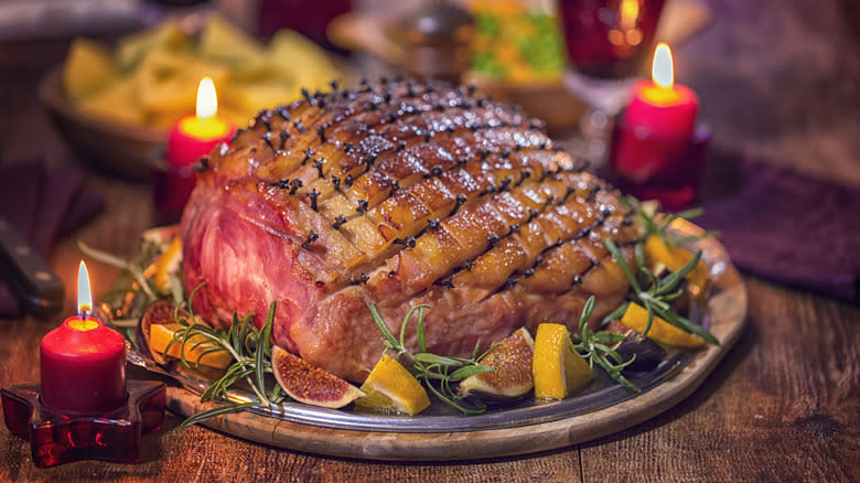 Glazed ham with figs and oranges on table with candles