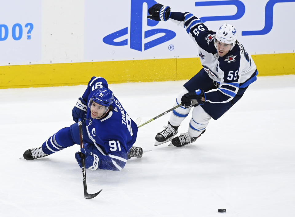 Toronto Maple Leafs center John Tavares (91) is tripped by Winnipeg Jets center Mark Scheifele (55) during first-period NHL hockey game action in Toronto, Saturday, March 13, 2021. (Frank Gunn/The Canadian Press via AP)