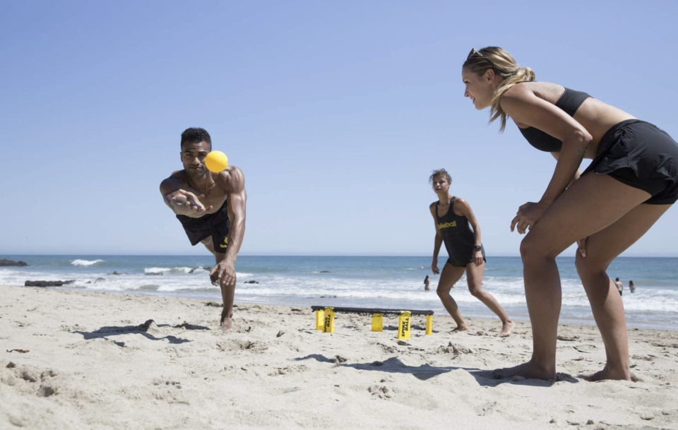 three people on sandy beach playing spikeball