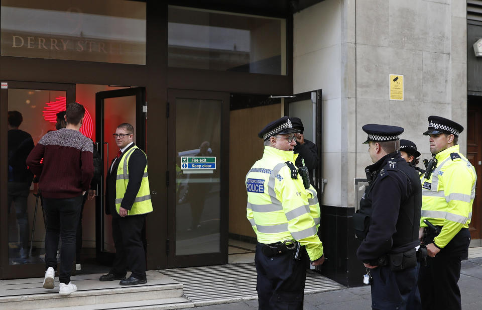 Police officers and security watch as people re-enter a building after a stabbing incident in central London, Friday, Nov. 2, 2018. British police say two people have been stabbed and a man has been arrested at an address in central London that is home to the offices of Sony Music. (AP Photo/Alastair Grant)