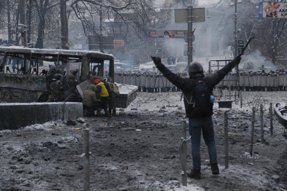 A protester gestures as others shield themselves behind a burned vehicle during a clash with police in central Kiev, Ukraine, early Wednesday, Jan. 22, 2014. Two people have died in clashes between protesters and police in the Ukrainian capital Wednesday, according to medics on the site, in a development that will likely escalate Ukraine’s two month-long political crisis. (AP Photo/Sergei Grits)