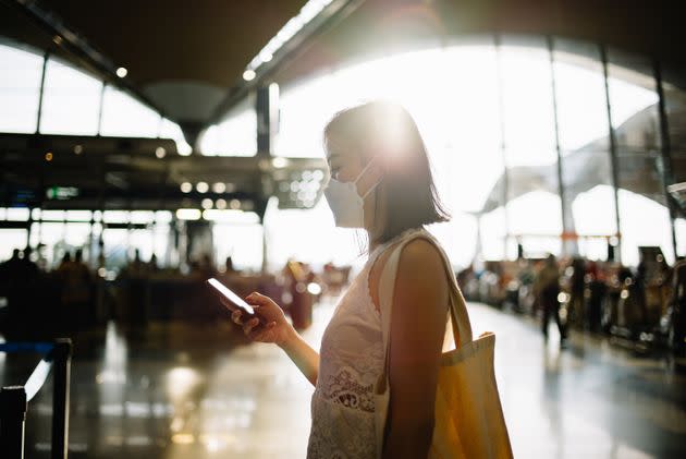 Image of an Asian Chinese woman using with protective face mask using smartphone at airport terminal (Photo: hxyume via Getty Images)