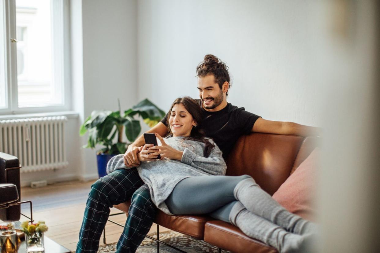 young couple with mobile phone relaxing on sofa