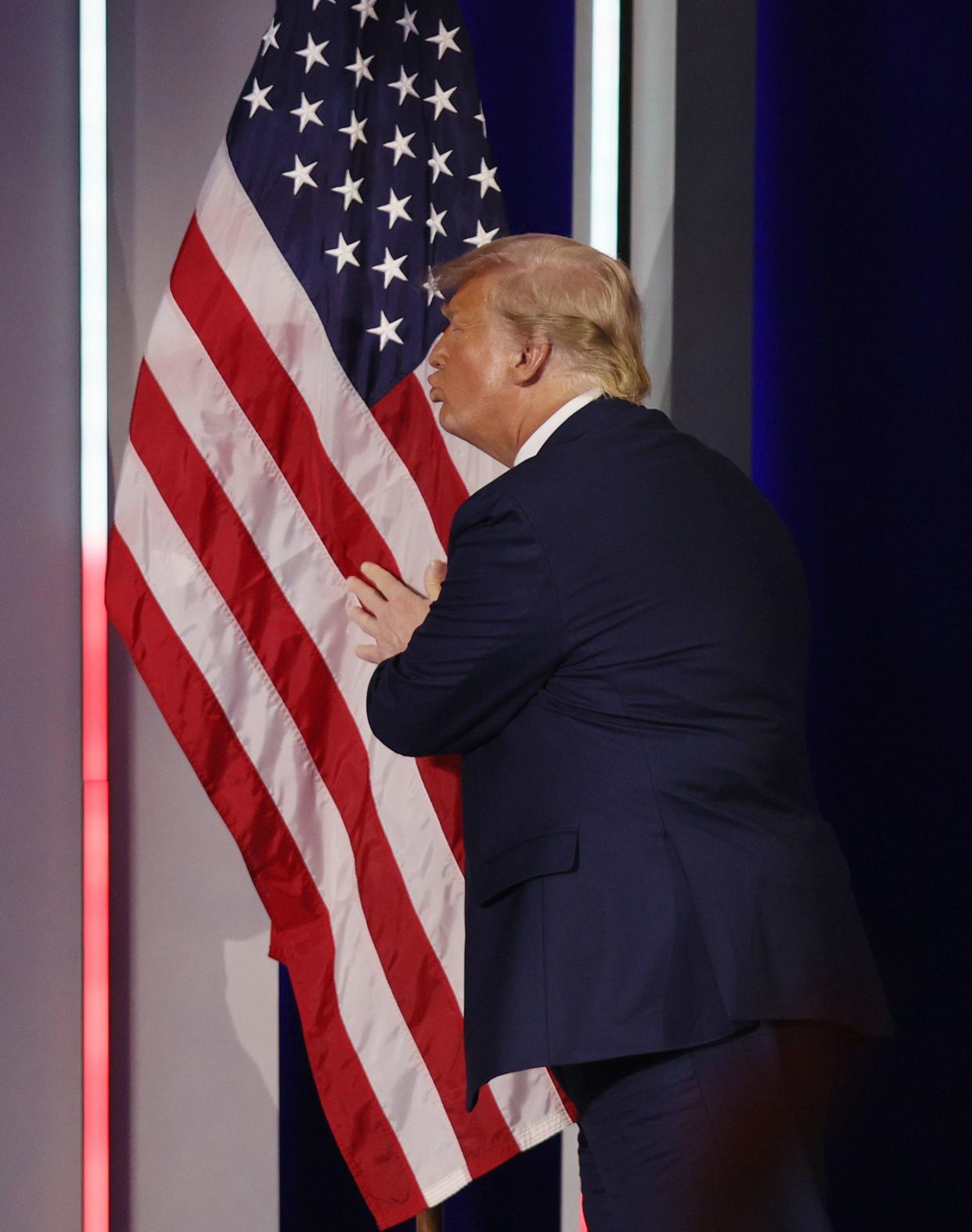 Former President Donald Trump embraces the American flag as he arrives on stage to address CPAC on Sunday in Orlando, Fla. 