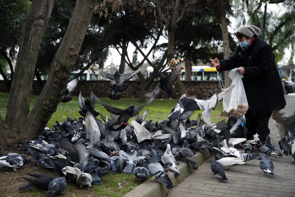 A woman wearing a face mask to prevent the spread of coronavirus, feeds pigeons at a park in Athens, Friday, Jan. 22, 2021. Greece's government has extended nationwide lockdown measures indefinitely as a nightly curfew, domestic travel restrictions and stay-at-home orders will all remain in effect after being first imposed in early November. (AP Photo/Thanassis Stavrakis)