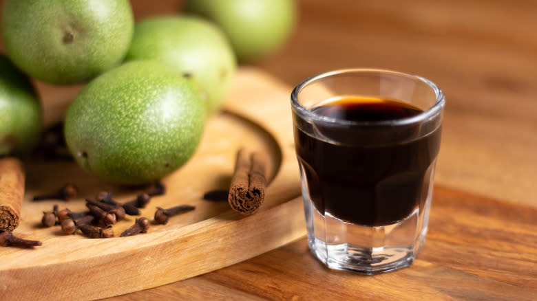 glass of nocino on table next to green walnuts