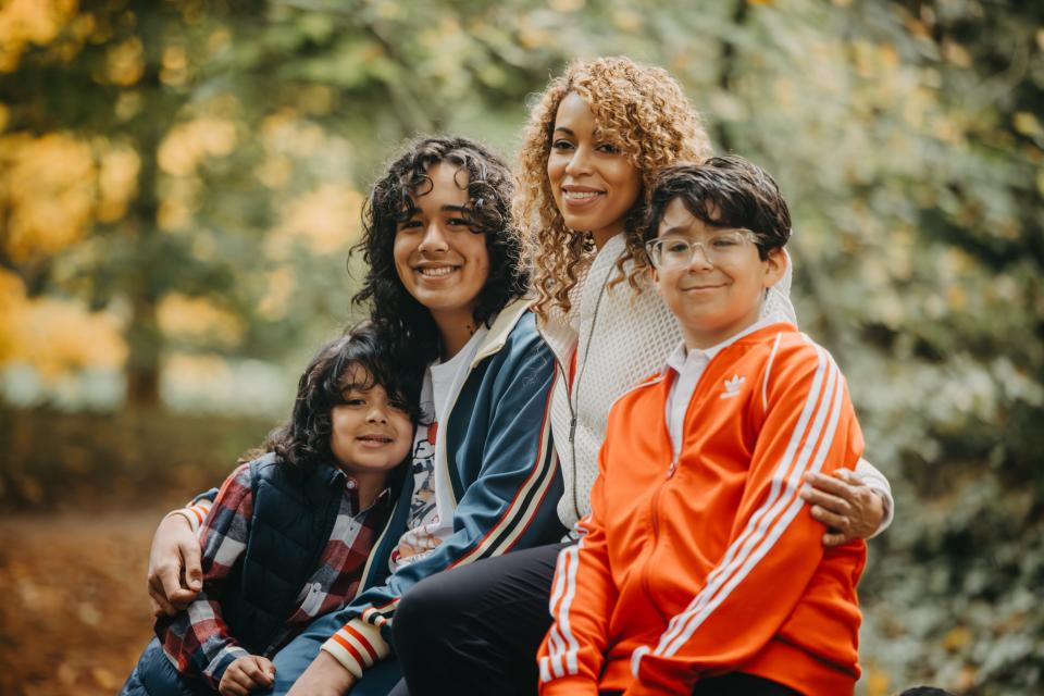 Chezik Tsunoda with her three sons, smiling and staring at the camera, while outdoors on a sunny day.