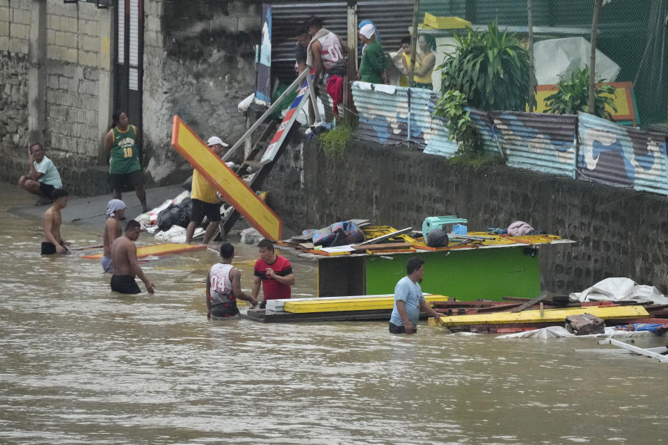 Workers transfer construction materials to higher grounds along a swollen river due to enhanced rains brought about by Typhoon Doksuri on Thursday, July 27, 2023, in Marikina city, Philippines. Typhoon Doksuri lashed northern Philippine provinces with ferocious wind and rain Wednesday, leaving several people dead and displacing thousands of others as it blew roofs off houses, flooded low-lying villages and triggered dozens of landslides, officials said. (AP Photo/Aaron Favila)