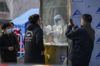 A man uses a smartphone to record residents getting a throat swab at a mass coronavirus test site in Xichen District in Beijing, Tuesday, Jan. 25, 2022. Hong Kong has already suspended many overseas flights and requires arrivals be quarantined, similar to mainland China's "zero-tolerance" approach to the virus that has placed millions under lockdowns and mandates mask wearing, rigorous case tracing and mass testing. (AP Photo/Andy Wong)