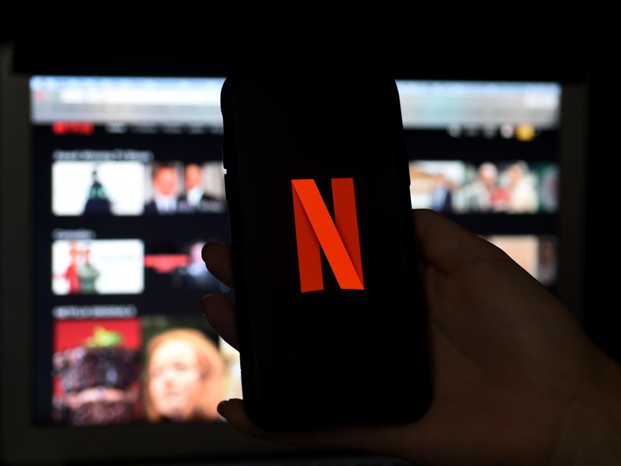 A phone is held before a TV bearing the Netflix corporate logo (AFP via Getty Images)