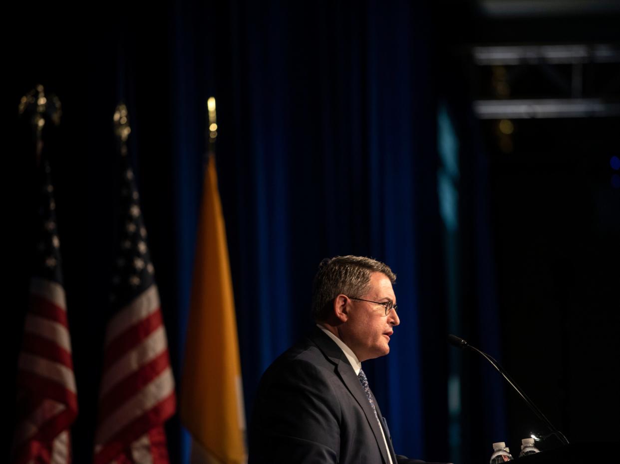 Leonard A. Leo speaks to an audience at a podium with American flags behind him