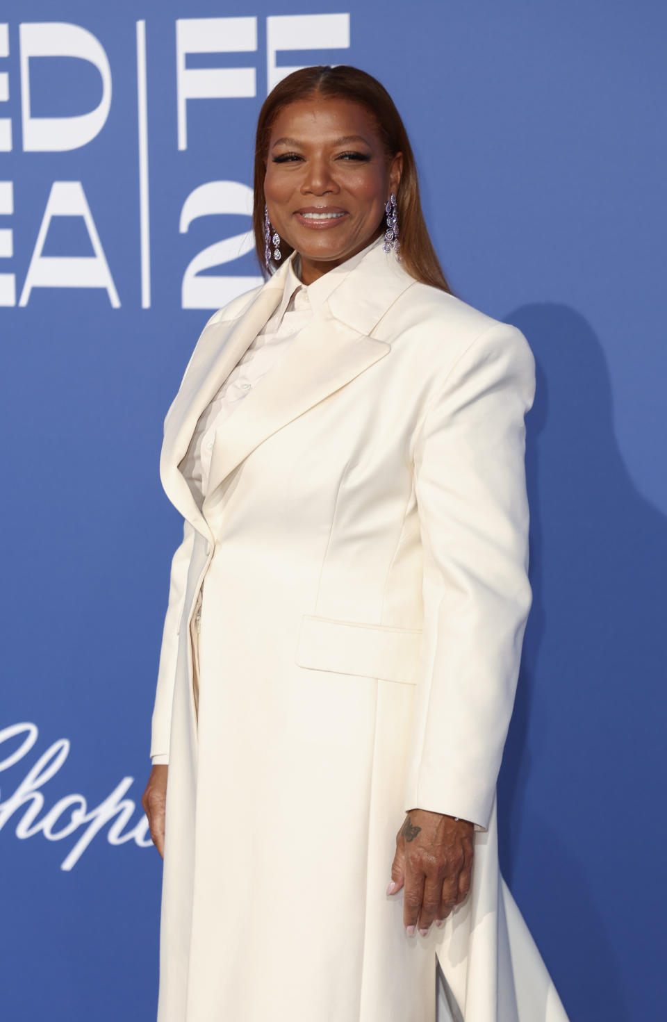 Queen Latifah poses on the red carpet in a formal white suit with long coat at a celebrity event