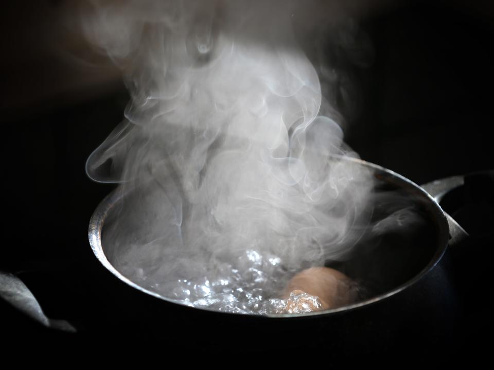 An egg lies in a pot on a hotplate in boiling water.