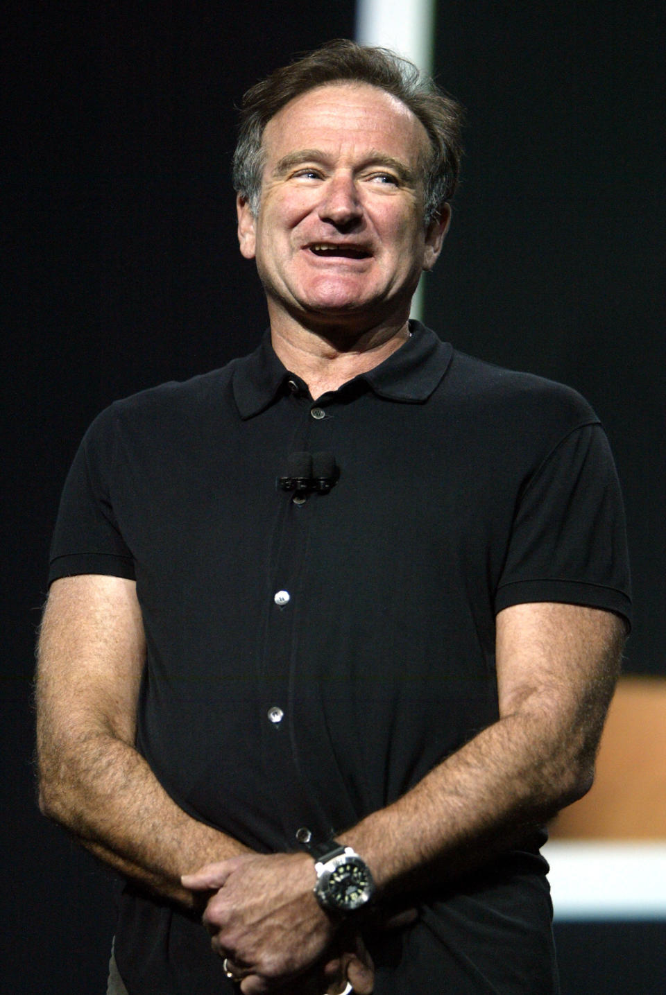 Robin Williams standing with his hands folded talking