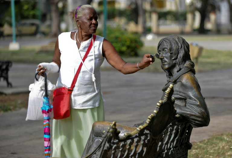 A woman puts glasses on a statue of John Lennon, in a park in Havana, on March 11, 2017