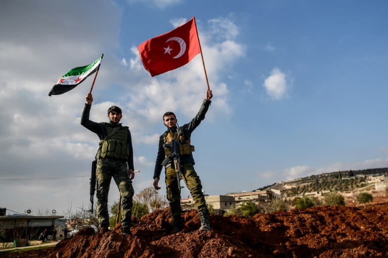 Ankara-backed Syrian rebel fighters hold up Turkish and Free Syrian Army flags on a road leading to Afrin