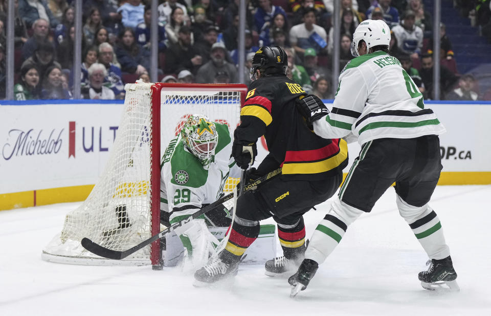 Dallas Stars goalie Jake Oettinger (29) stops Vancouver Canucks' Brock Boeser (6) as Stars' Miro Heiskanen (4) defends during the third period of an NHL hockey game Thursday, March 28, 2024, in Vancouver, British Columbia. (Darryl Dyck/The Canadian Press via AP)