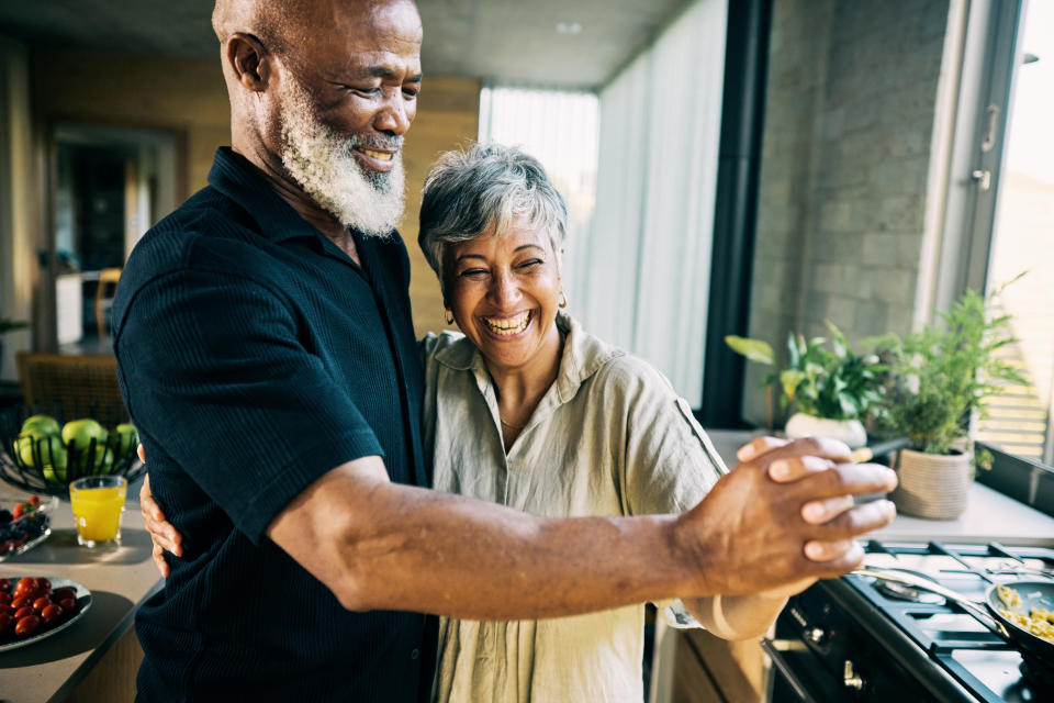 An elderly couple, smiling and dancing in their kitchen, enjoying a lighthearted moment together