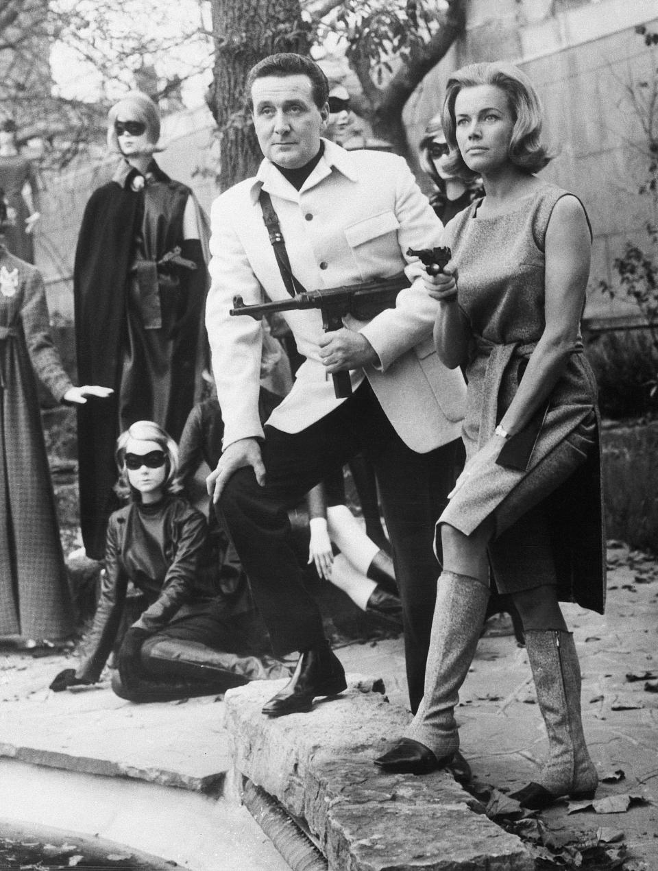 (Original Caption) 11/8/1963-London, England- Looking very dangerous as leaders of a masked gang, Honor Blackman and Patrick MacNee stand well armored. Actually, the couple star in the British adventure TV series, "The Avengers," and are demonstrating why their fashions were inspired by the characters they portray. Their ensembles were designed by Frederick Starke and Hardy Amies.