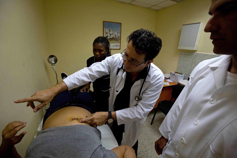 In this March 27, 2014 photo, Omar Fernandez, a Cuban doctor, examines a patient at a medical center in the Petare shanty town of Caracas, Venezuela. Cuban doctors offer free emergency, ophthalmology and pediatric care, as well as minimally invasive surgical procedures. Some also minister to gunshot victims and drug and alcohol addicts. (AP Photo/Fernando Llano)