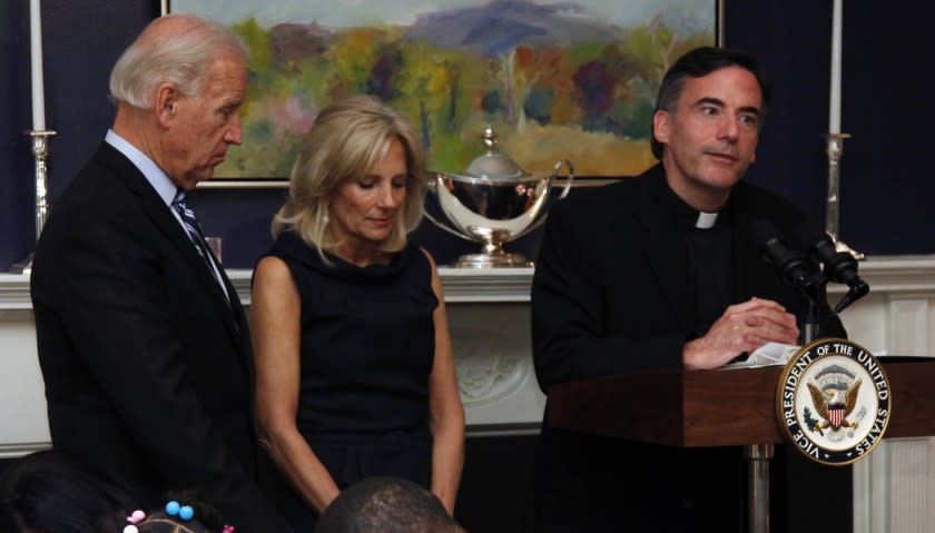 FILE - In this Nov. 22, 2010, file photo, Vice President Joe Biden, left, and his wife, Jill Biden, center, stand with heads bowed as the Rev. Kevin O'Brien says the blessing during a Thanksgiving meal for Wounded Warriors in Washington. O'Brien, the Jesuit priest who presided over an inaugural Mass for President Joe Biden, is under investigation for unspecified allegations and is on leave from his position as president of Santa Clara University in Northern California, according to a statement from the college's board of trustees. (AP Photo/Carolyn Kaster, File)