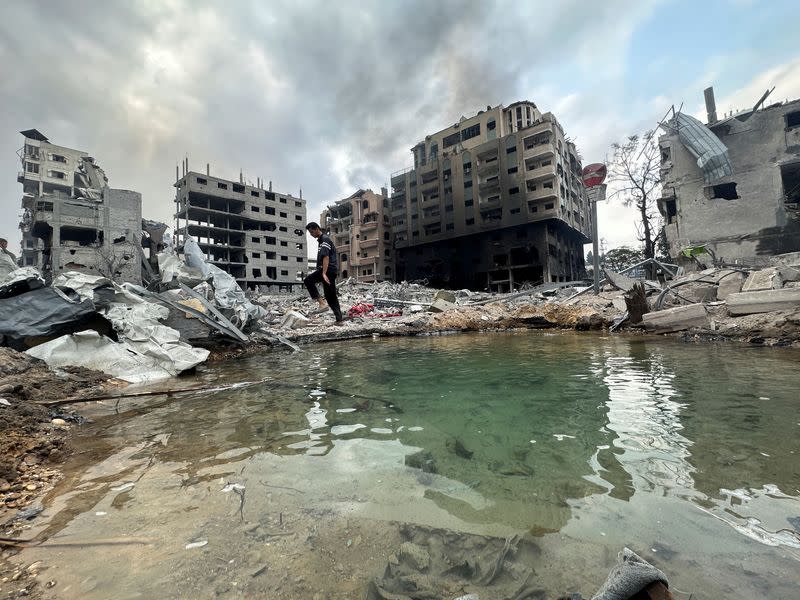 Un palestino camina entre los escombros mientras sale humo de un edificio residencial dañado cercano, tras los ataques israelíes, en Gaza