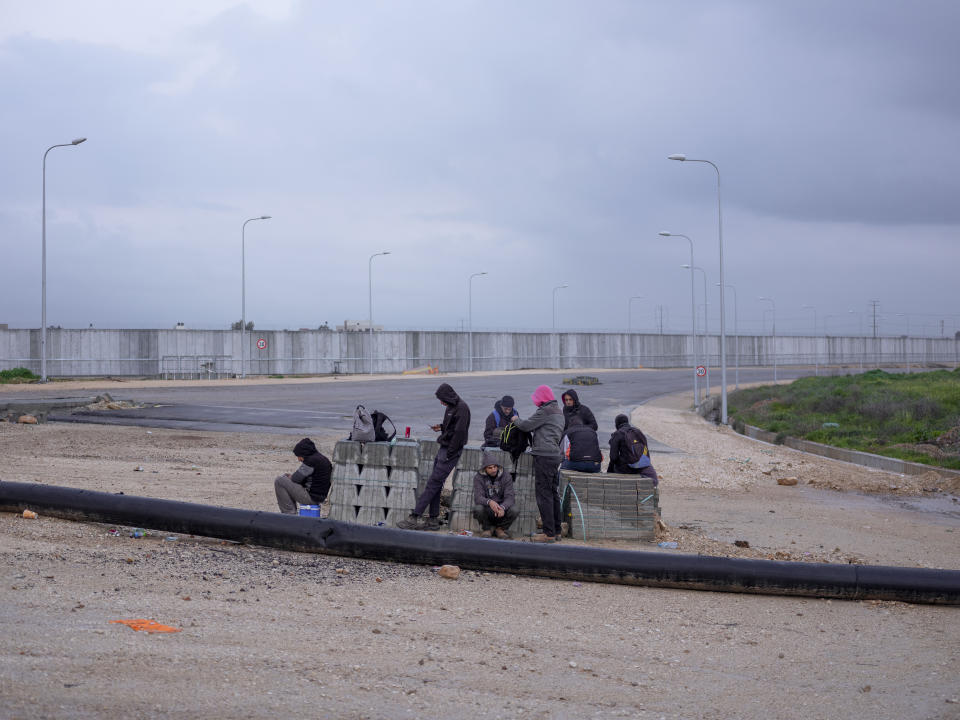 Palestinian laborers wait for transportation after crossing into Israel from the West Bank at Eyal crossing between the West Bank town of Qalqilya and the Israeli Kibbutz Eyal Sunday, Feb. 20, 2022. Twenty years after Israel decided to built its controversial separation barrier amid a wave of Palestinian attacks, it remains in place, even as Israel encourages its own citizens to settle on both sides and admits tens of thousands of Palestinian laborers. (AP Photo/Oded Balilty)