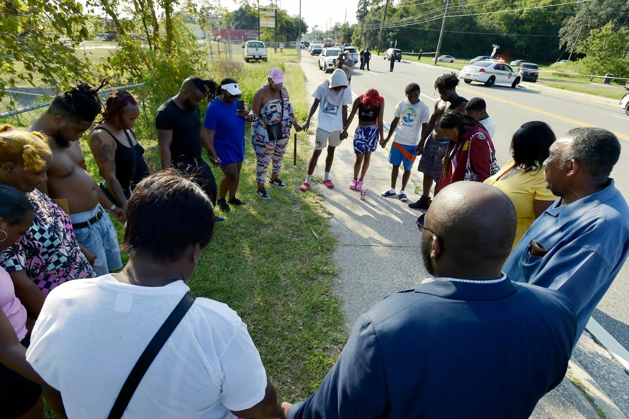 Pastor Lee Harris (far right) of Mt. Olive Primitive Baptist Church leads a prayer with neighbors down the street from where investigators were collecting evidence at the Dollar General store on Kings Road in Jacksonville on Aug. 26. Earlier that day, a white individual shot and killed a Black woman and two Black men at the store, then took his own life using an AR-15 style rifle with swastikas and other white nationalist markings on it.