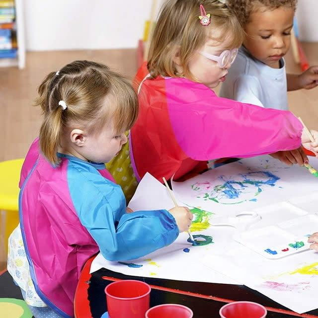 two children with smocks on creating artwork