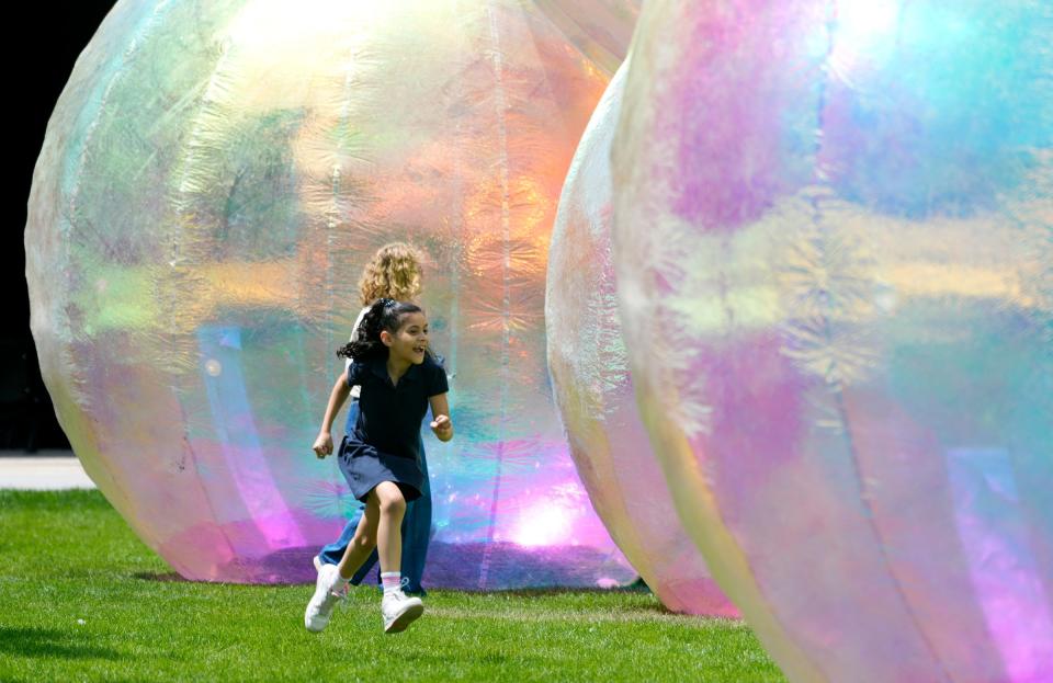Valentina Nieves, 8, who was with her mother, Karleen Cortes, of Hales Corners, runs into an opening under a bubble at the Evanescent bubble exhibit outside the Marcus Performing Arts Center in  Milwaukee on Monday, July 17, 2023. The exhibit consists of three sets of four bubbles each made from a color-reflecting material that reacts to the changing light of the sun as it moves across the sky.