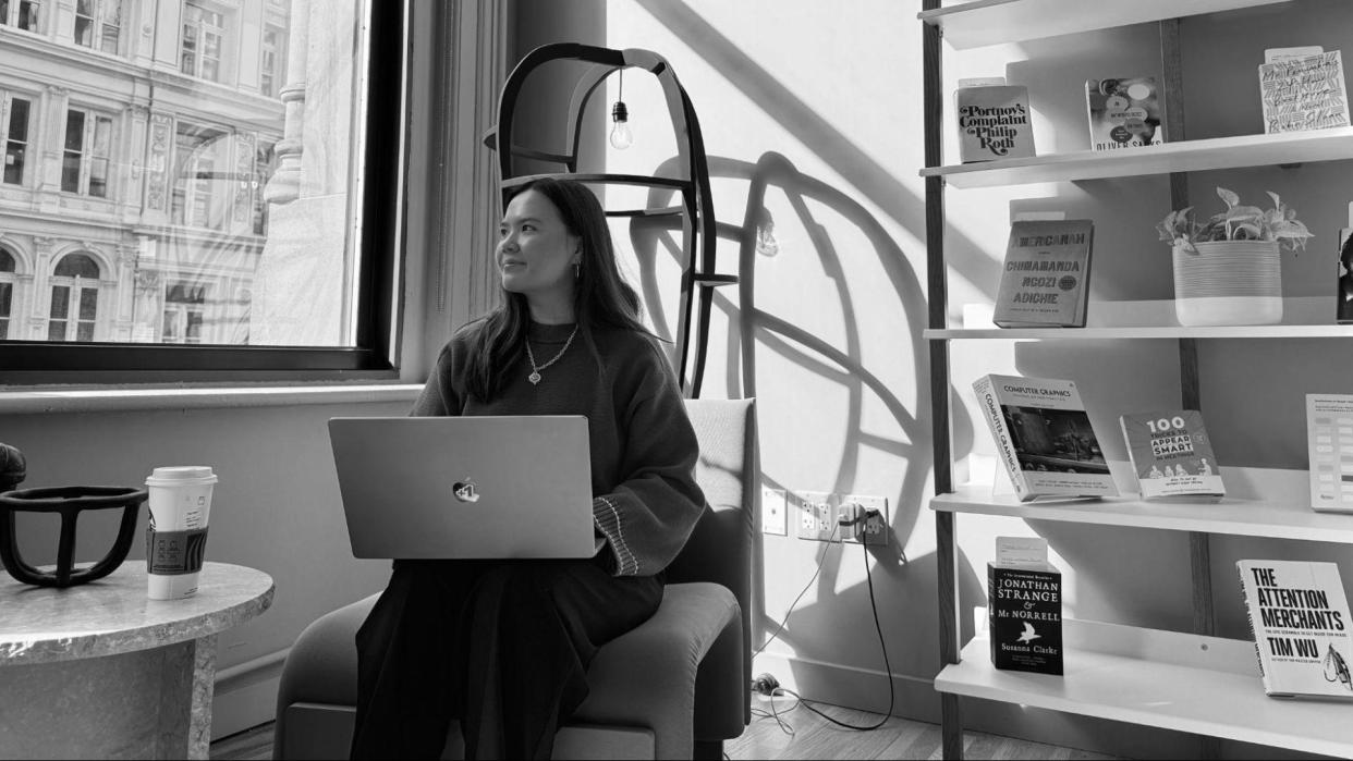  Image of a woman with a laptop with a bookcase behind her. 