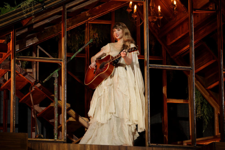 Taylor Swift performs on stage with a guitar, wearing a ruffled dress