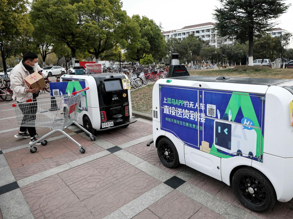 A Chinese consumer wearing a light-colored jacket removes a package from a rectangular autonomous delivery robot.