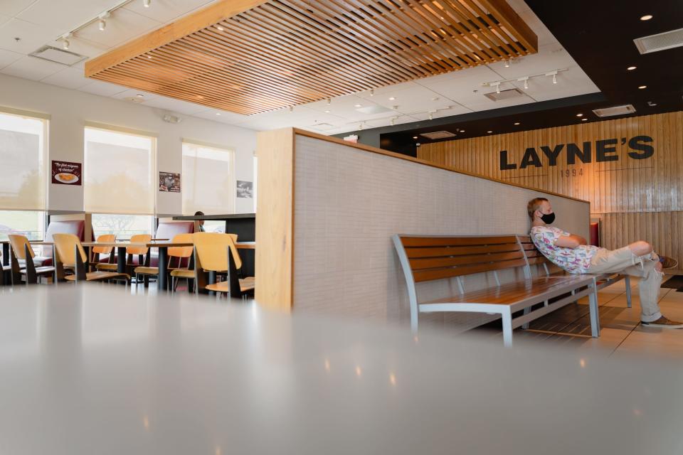 A customer wearing a white shirt sits on a bench in a fast food restaurant against a white wall.