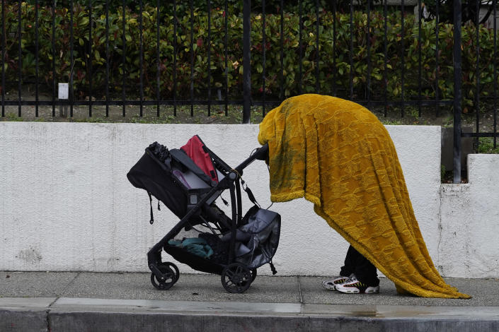 A homeless person shields themselves from the rain under a wet cover in downtown Los Angeles Tuesday, Dec. 14, 2021, in Los Angeles. A powerful storm slid south through California on Tuesday, drenching the drought-stricken state with desperately needed rain. (AP Photo/Damian Dovarganes)