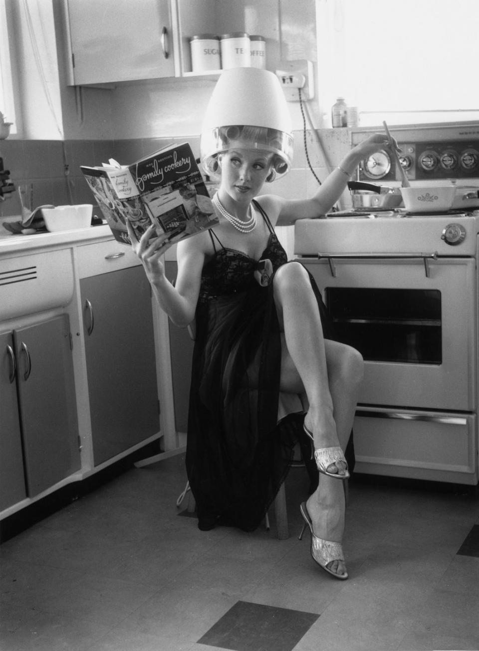 <p>Actress Barbara Roscoe demonstrates her multitasking skills at home in 1963, as she mans the stove while drying her hair. </p>