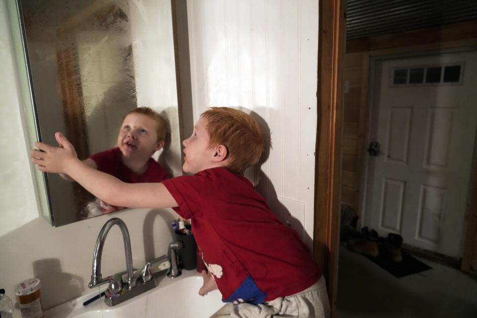 Waylon Prince wipes condensation off of a mirror after brushing his teeth before bed at Camp Graves, a nonprofit helping provide temporary housing, Tuesday, Jan. 16, 2024, in Water Valley, Ky. Two years after the tornado outbreak that killed dozens and leveled much of the real estate in Mayfield, many people, like the Prince family, are still living through another, slower disaster, the search for housing. (AP Photo/Joshua A. Bickel)