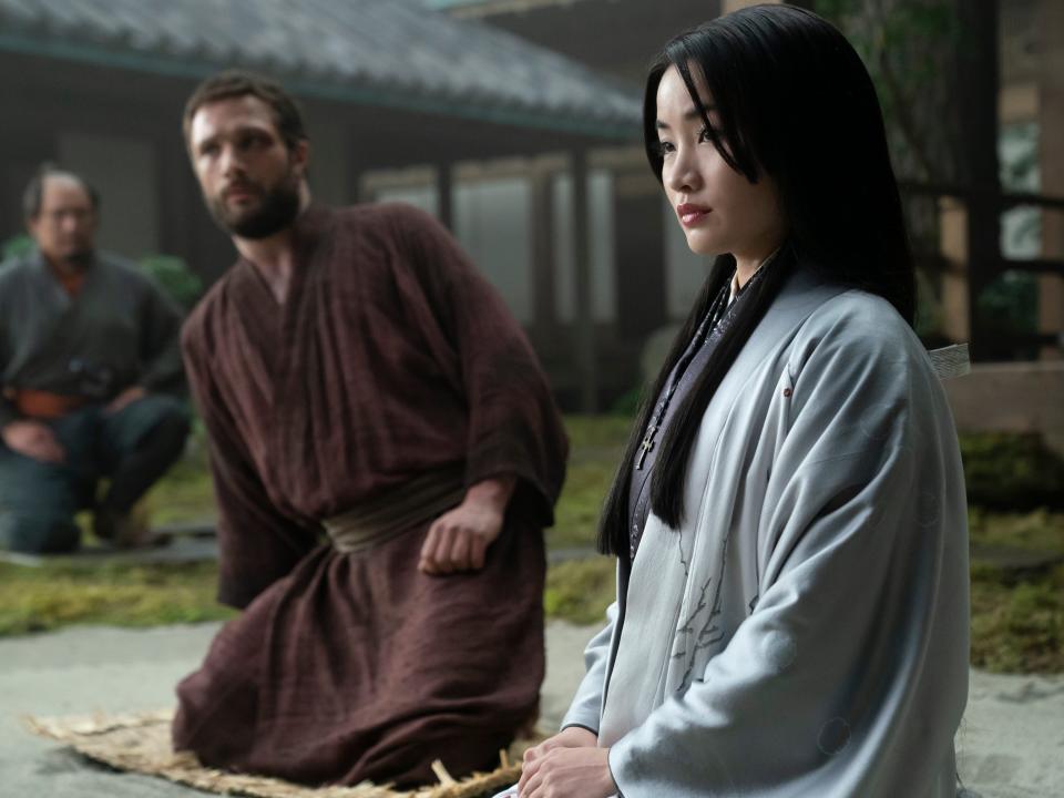 toda mariko and john blackthorne, sitting together in a courtyard. mariko is wearing white robes, blackthorne in red ones