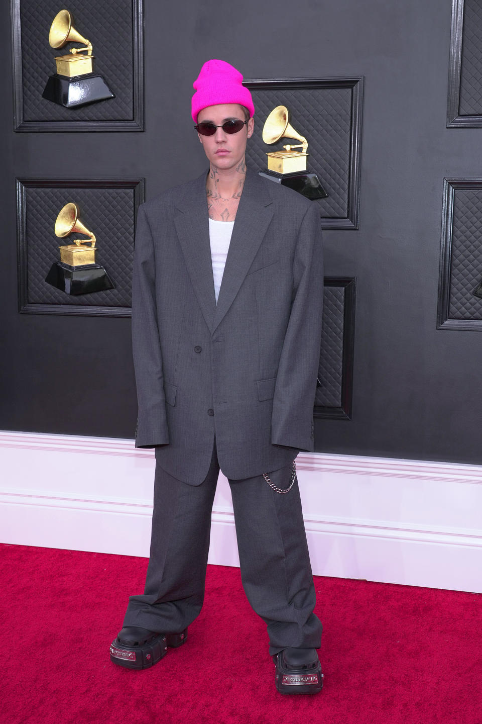 Justin Bieber on the red carpet in an oversized gray suit, white shirt, pink beanie, and sunglasses at the Grammys