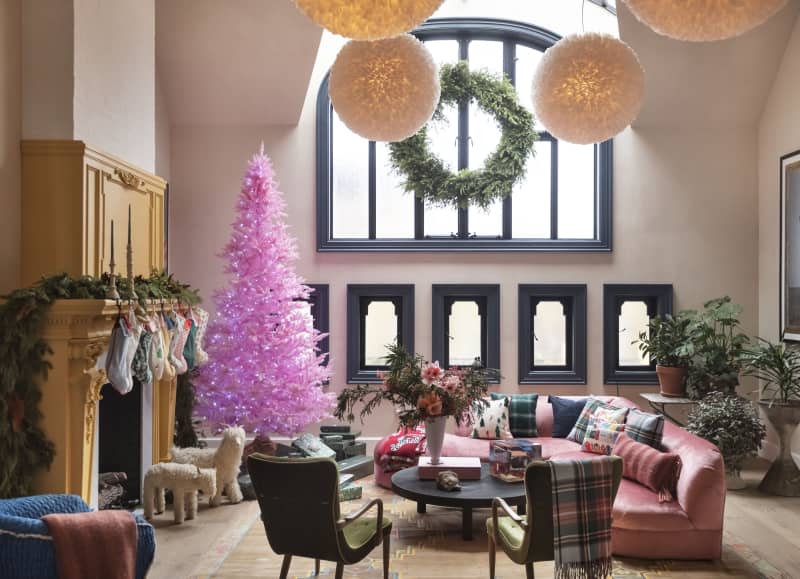 Stockings hang on a yellow fireplace in a living room with a large pink tree.