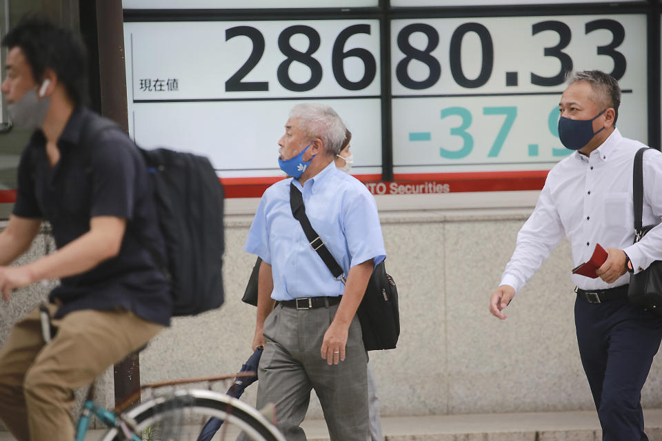 People wearing face masks to help protect against the spread of the coronavirus pass by an electronic stock board of a securities firm in Tokyo, Wednesday, July 14, 2021. (AP Photo/Koji Sasahara)